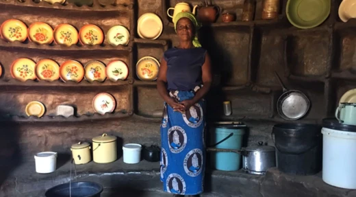Vrouw in traditionele kleding in een keuken met serviesgoed in Malawi