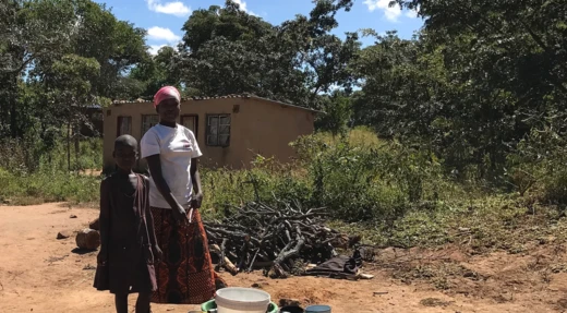 Vrouw met kind bij een huis en een stapel brandhout in Malawi