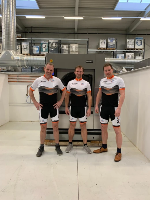Drie medewerkers van Laundry Expert in wielershirt van Team HardenbergOp bij een wasmachine