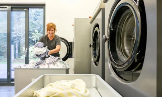 Medewerkster met wasgoed bij een professionele wasmachine