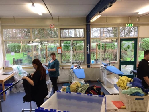 Medewerksters strijken en vouwen wasgoed aan strijktafels