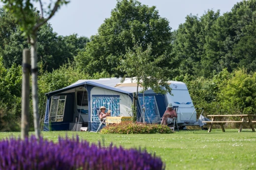 Camping met caravan onder een luifel en mensen die buiten zitten