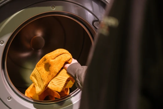 Medewerker haalt een oranje handdoek uit een professionele wasdroger