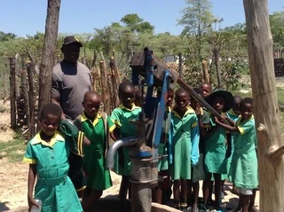 Schoolkinderen bij een waterpomp in Malawi, begeleid door een man